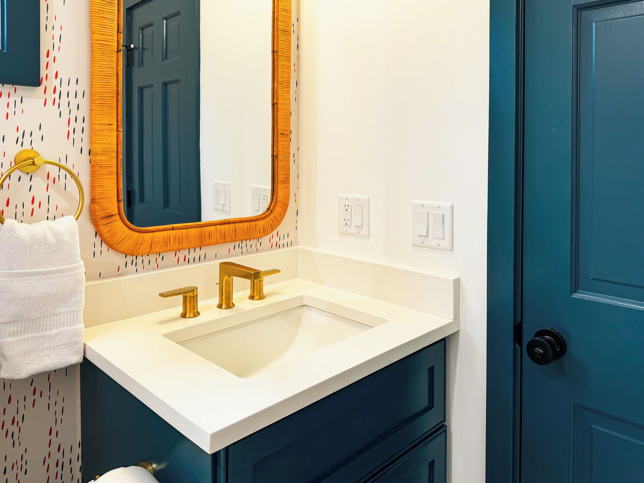 A bathroom with a white sink, gold faucets, a mirror with a wooden frame, and a blue door.