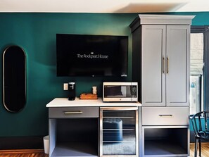 A compact kitchenette with a microwave, coffee maker, and a flat-screen TV displaying 'The Rockport House'.