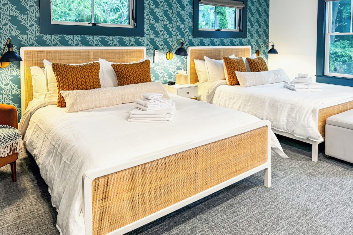 Une chambre d’hôtel avec deux lits, chacun doté d’une tête de lit en osier, de linge de lit blanc et d’une petite table de chevet avec une lampe.