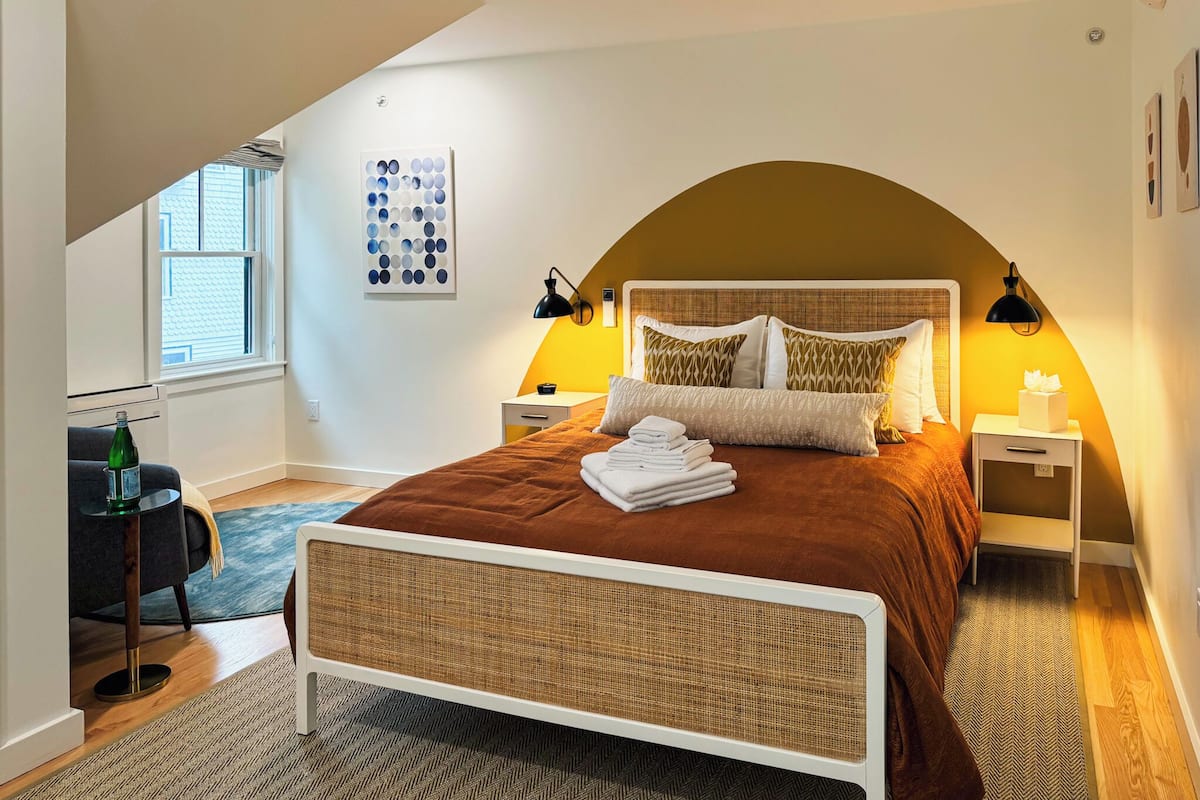 Une chambre à coucher comprenant un lit, deux tables de chevet, une lampe sur pied, une œuvre d’art murale et une fenêtre.