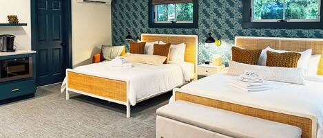 A hotel room with two beds, a kitchenette, and a view of trees through the windows.