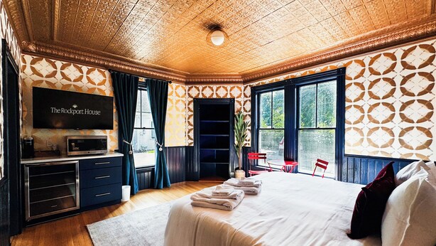 Ein Hotelzimmer mit einem großen Bett, einem Fernseher, einem Schreibtisch mit Computer und einem Fenster mit Vorhängen.