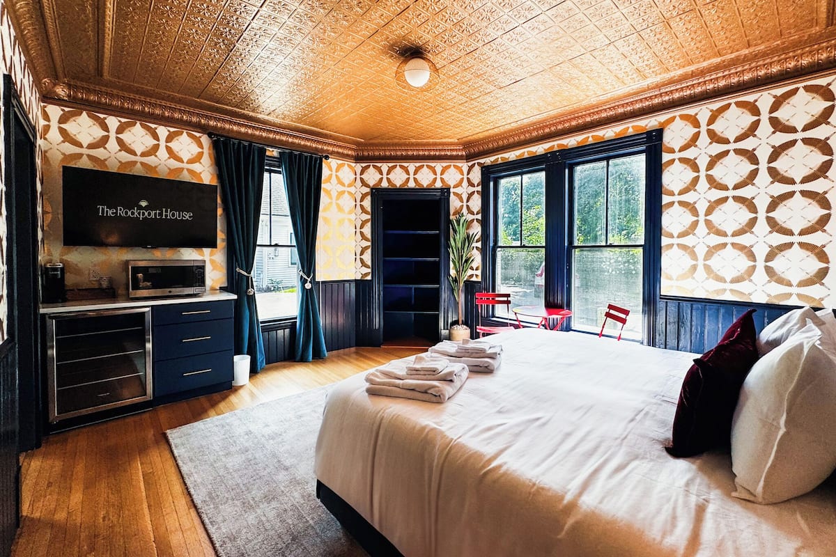 Une chambre d’hôtel avec un grand lit, une télévision, un bureau avec un ordinateur et une fenêtre avec des rideaux.