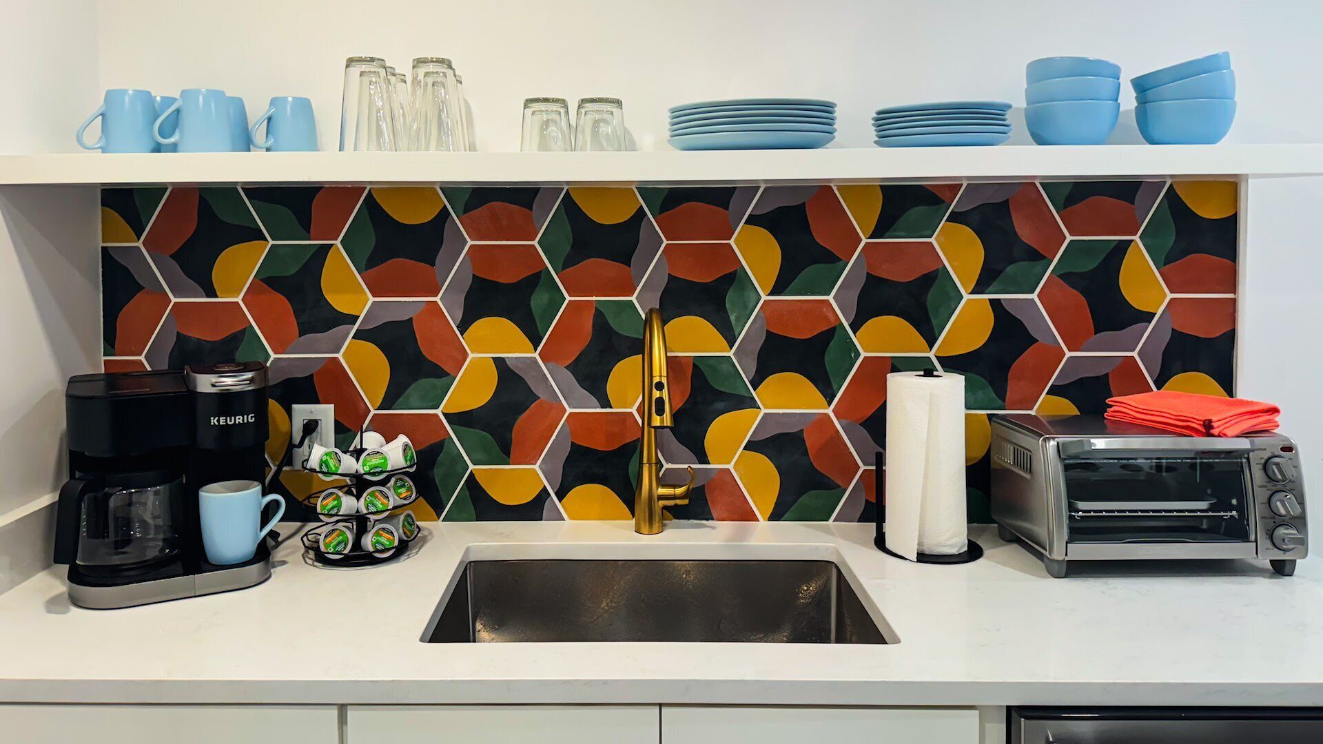 A kitchen with a colorful hexagonal backsplash, a coffee maker, a toaster, and various kitchen items.