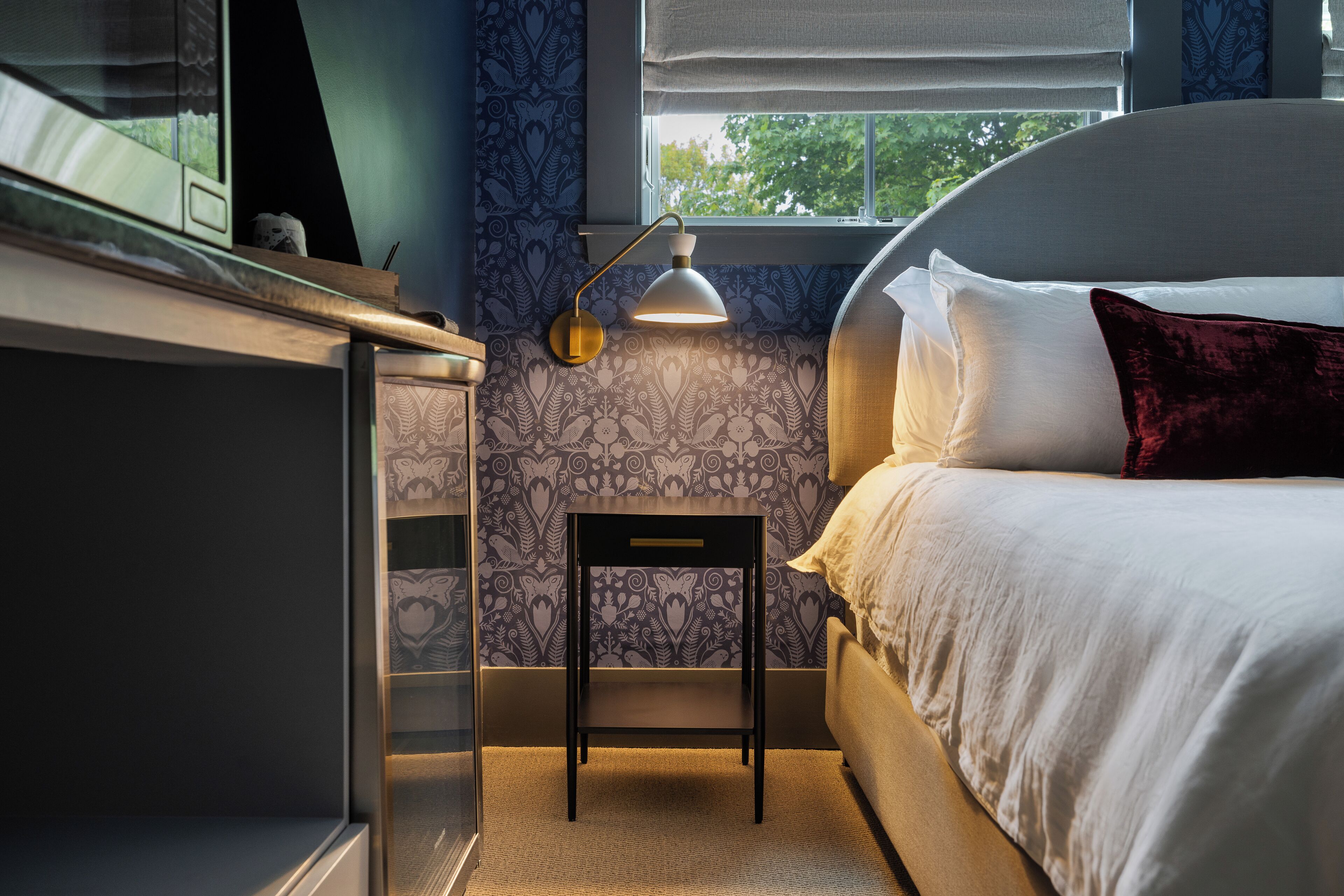 Une chambre à coucher comprenant un lit, un bureau, une chaise, une lampe et une fenêtre avec des stores.