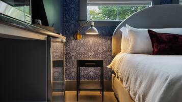 A bedroom with a bed, a desk, a chair, a lamp, and a window with blinds.
