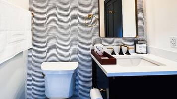 Un baño con cortina de ducha a rayas, inodoro, lavamanos con espejo y artículos de aseo.