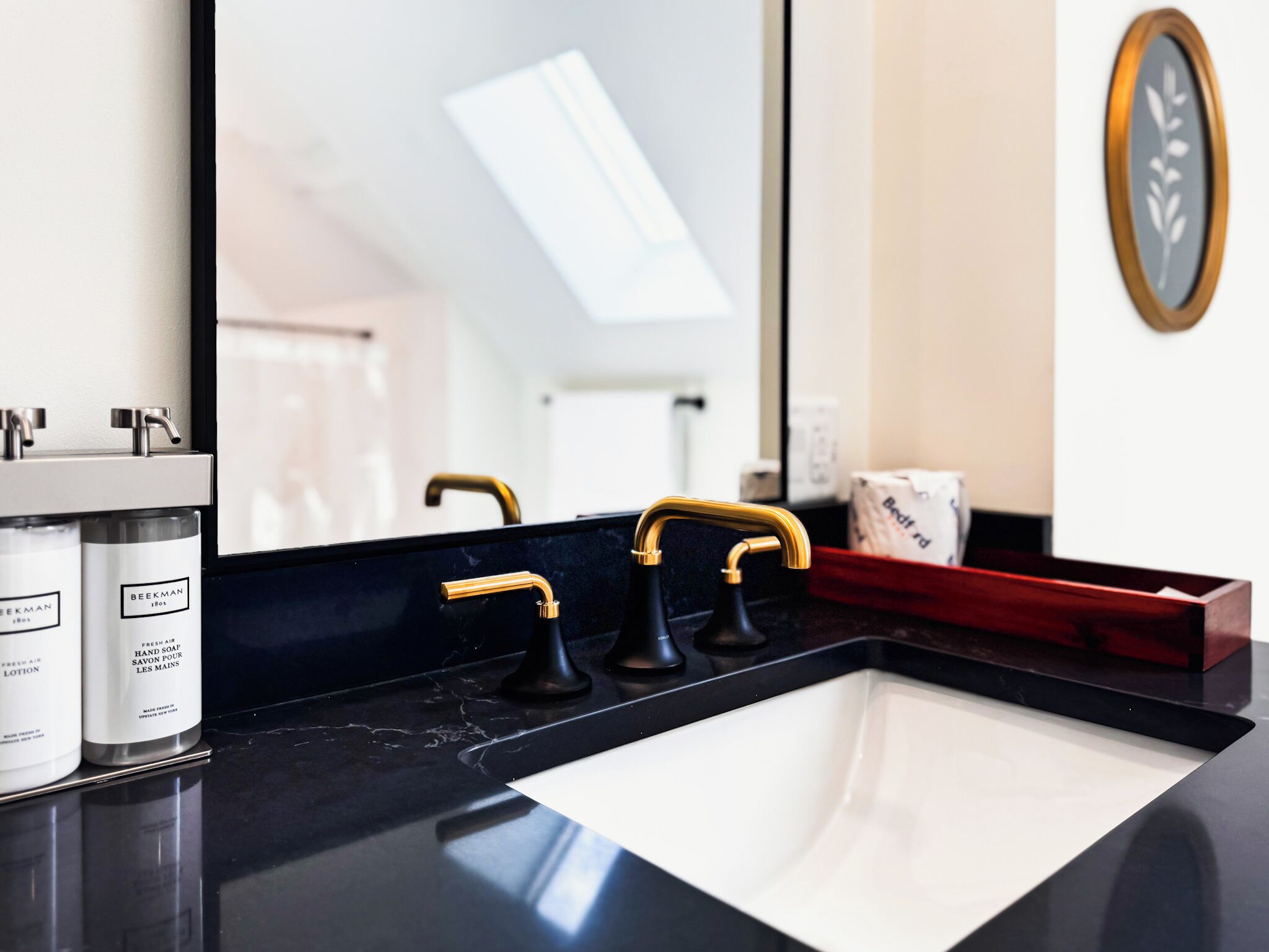 A modern bathroom with a black marble sink, gold faucets, and a large mirror.