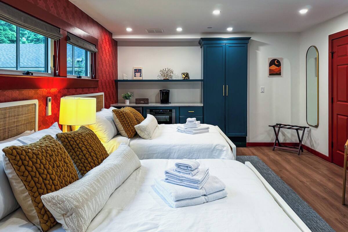 Une chambre d’hôtel avec deux lits, un bureau, une armoire et un miroir.