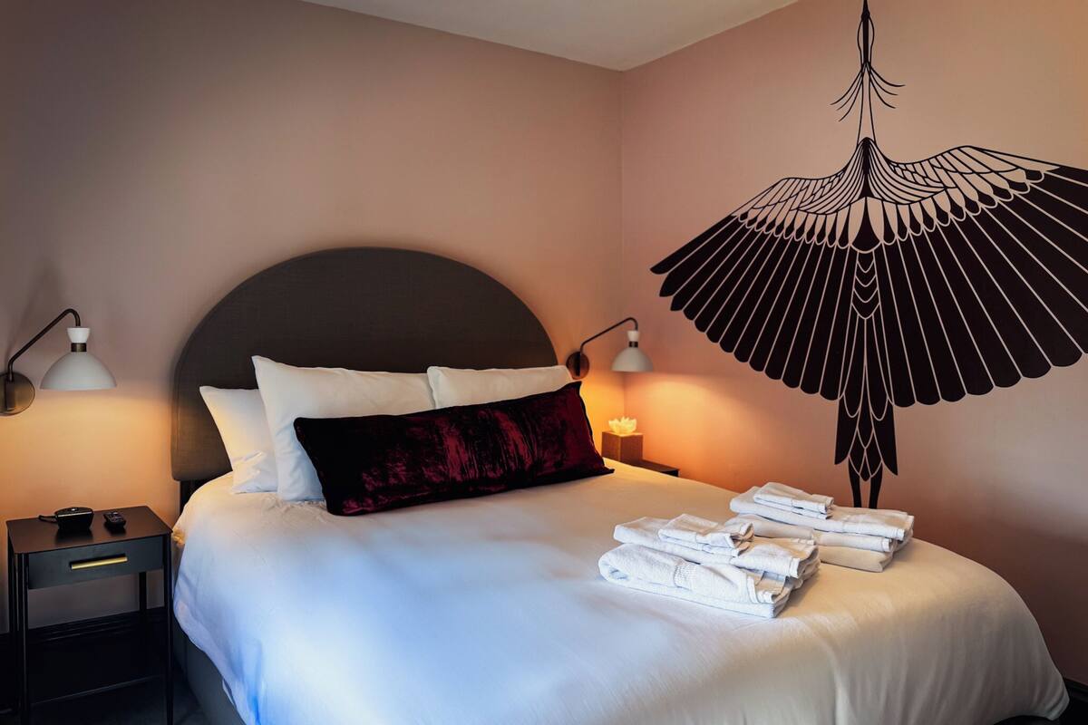 Un lit bien fait, avec du linge de lit blanc, une tête de lit sombre et un élément décoratif mural au-dessus.