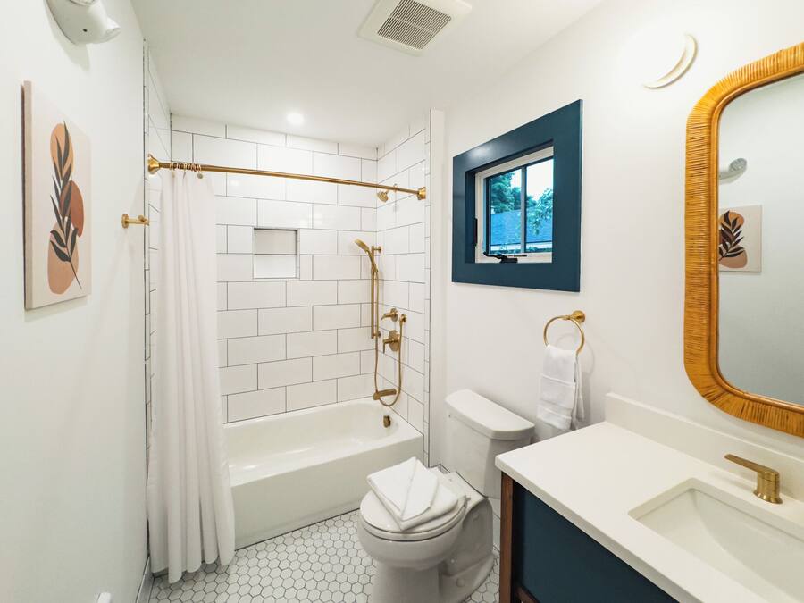 Ein Badezimmer mit einer weißen Badewanne, einer Toilette, einem Waschbecken und einer Dusche mit einer goldfarbenen Duschbrause.