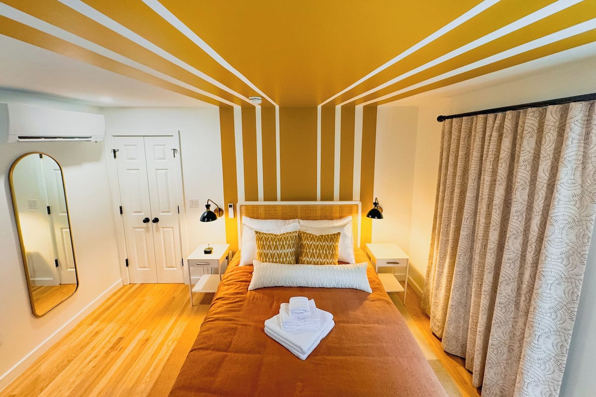 Une chambre d’hôtel avec un lit, des tables de chevet, un miroir et un rideau.
