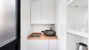 Un baño moderno con encimera de madera, lavamanos de piedra y un armario blanco en la parte superior.