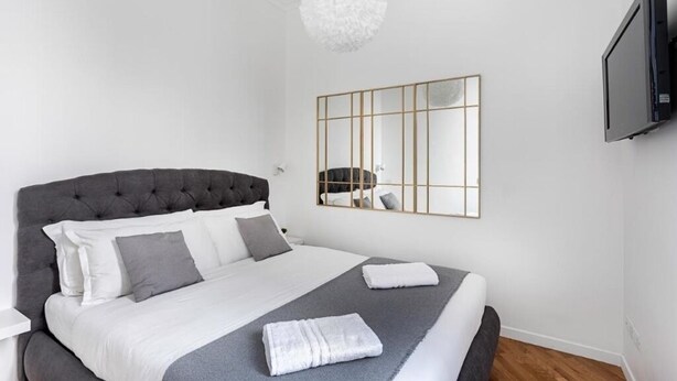 Un dormitorio con una cama grande, un televisor montado en la pared y una lámpara moderna.