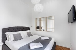 Een slaapkamer met een groot bed, een aan de muur bevestigde televisie en een moderne kroonluchter.