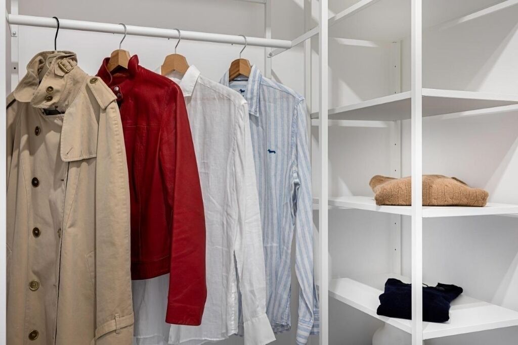 Um cabideiro com várias peças de vestuário e prateleiras com roupas dobradas.