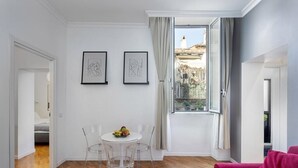 Una sala de estar moderna con piso de madera, una mesa redonda blanca con sillas, un sofá rojo y dos cuadros enmarcados en la pared.