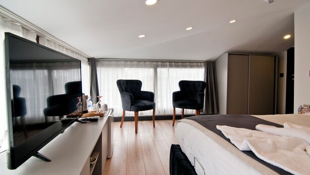 A modern hotel room with a flat-screen TV, a desk with a computer, two black armchairs, a bed with a white comforter, and a large wardrobe. - Demhat Hotel Old City (Istanbul)
