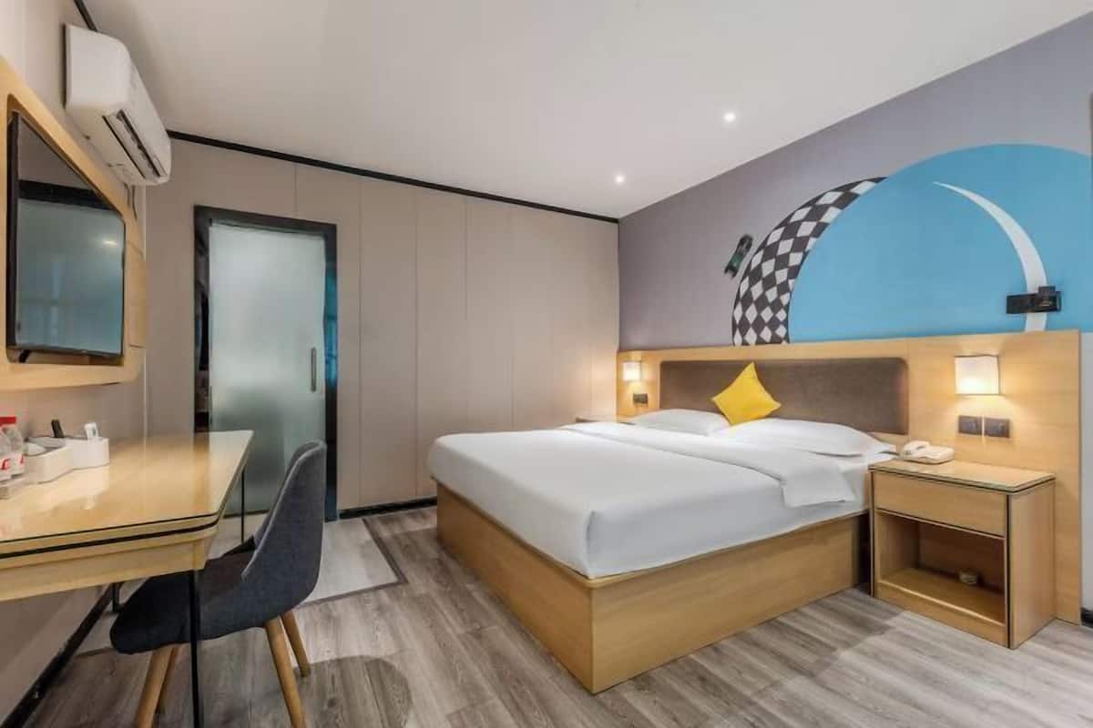 A hotel room with a bed, bedside table, chair, desk, and a wall with a checkered pattern.