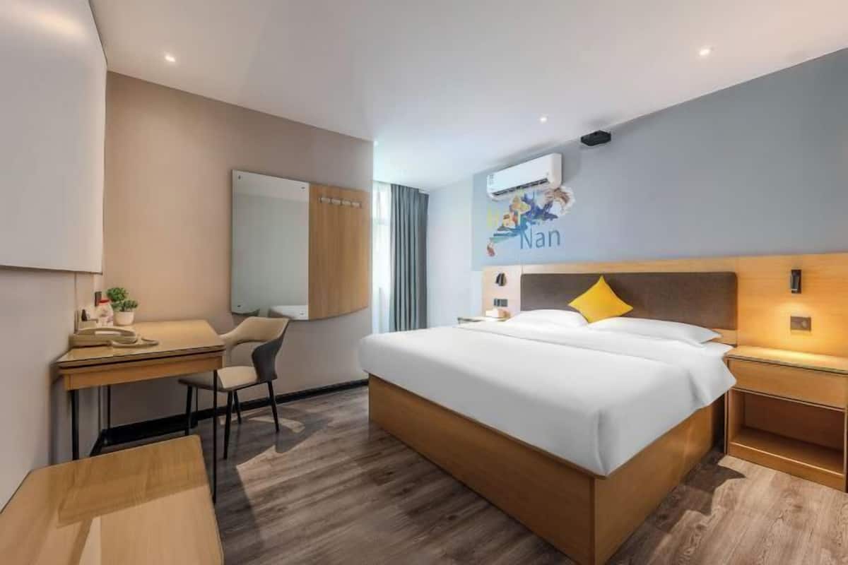 A modern hotel room with a bed, desk, chair, and a wall-mounted air conditioner.
