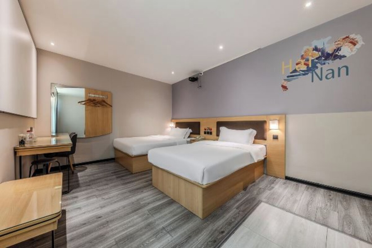 A hotel room with two beds, a desk, and a mirror.