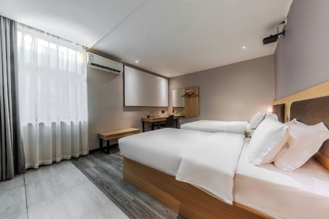 A hotel room with a bed, bedside table, desk, chair, and a large mirror.