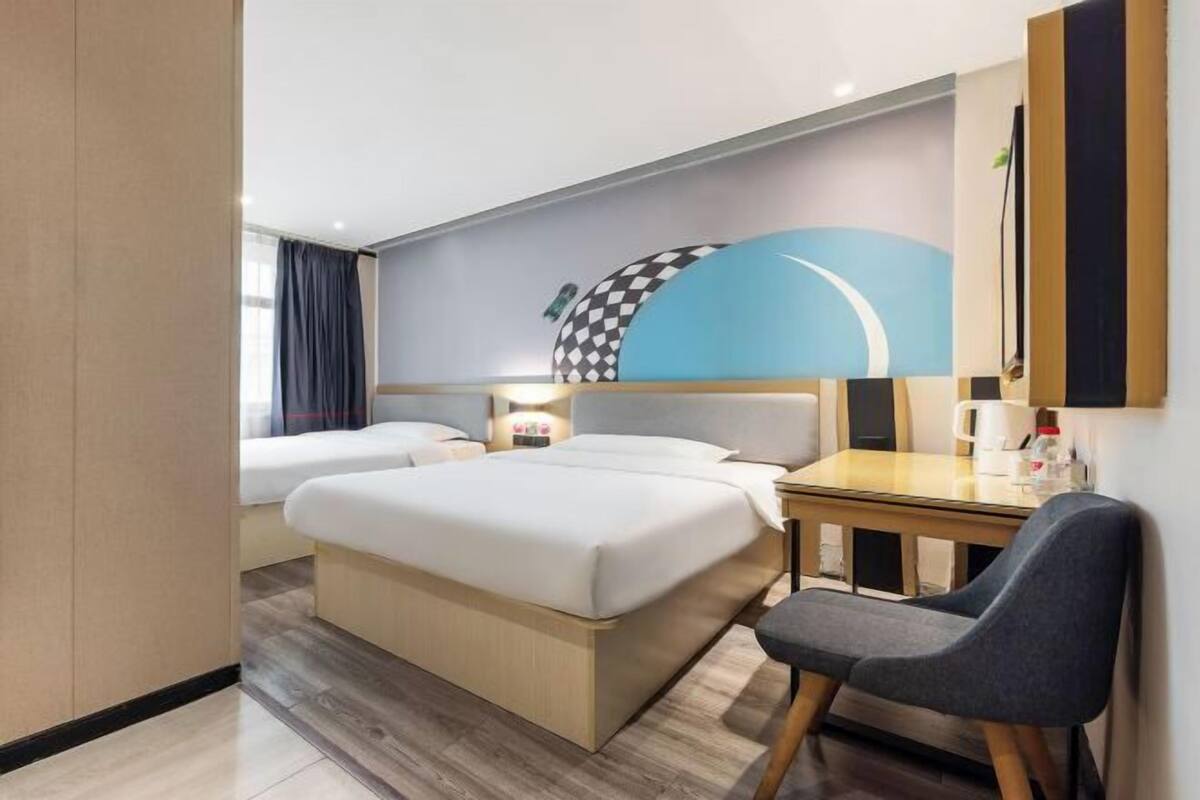 A hotel room with a bed, a desk, a chair, and a wall with a checkered pattern.
