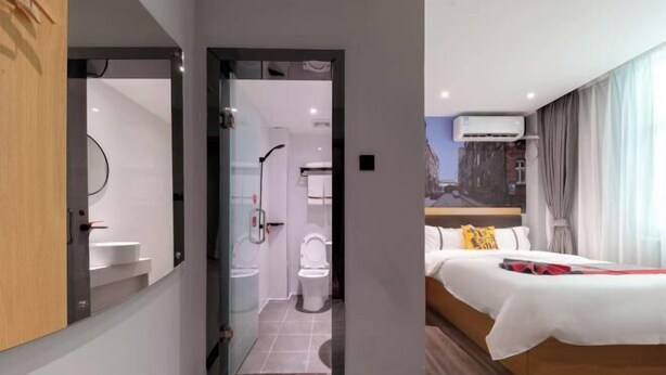 A modern hotel room with a large bed, a bathroom with a toilet and sink, and a view of the city through the window. - Courtyard by Marriott (Hainan College of Commerce and Industry Provincial Museum Store) (Haikou)