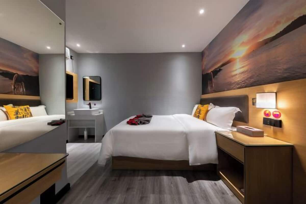 A modern hotel room with a bed, bedside table, mirror, and a painting on the wall.