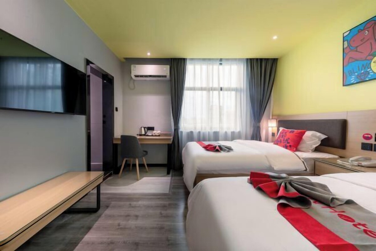 A hotel room with two beds, a desk, a TV, and a window with curtains.