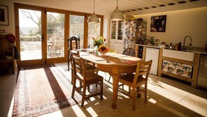 A dining area with a wooden table and chairs, a rug, and a view through large sliding glass doors to an outdoor patio. - Cotswolds Aonb-near Bath-sleeps8 (Bath)