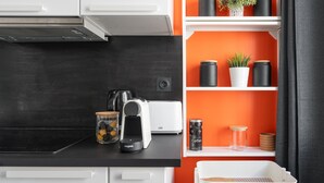A kitchen with a black countertop, a coffee maker, a toaster, and a shelf with jars and a potted plant.