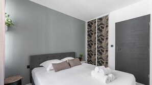 A modern bedroom with a grey headboard, white bedding, and a dark door.