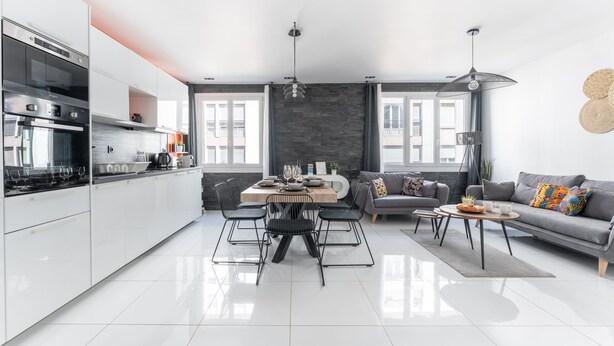 A modern kitchen with white cabinets, a built-in oven, and a dining area with a wooden table and chairs.