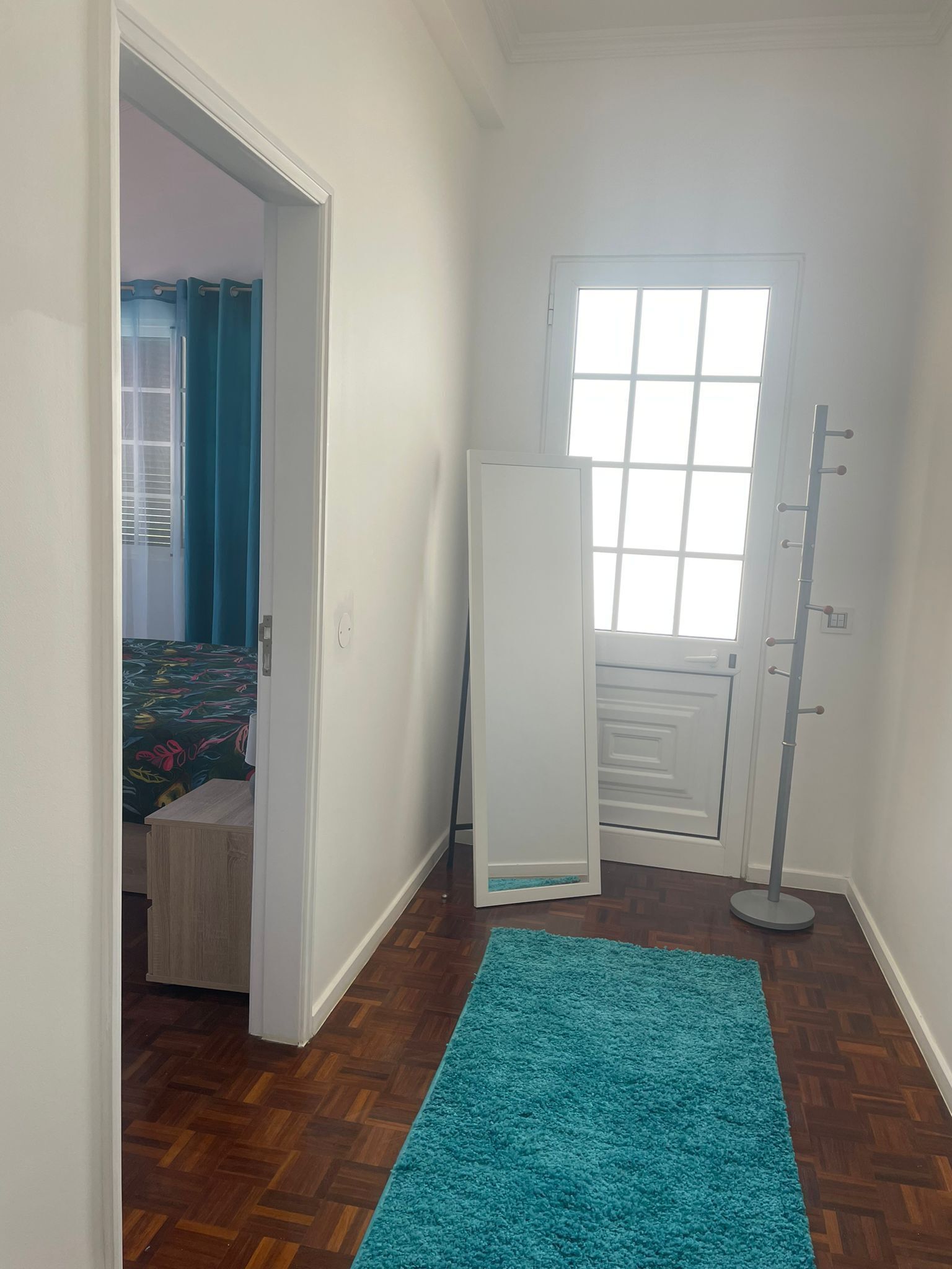 A room with a wooden floor, a teal rug, a door, and a window.