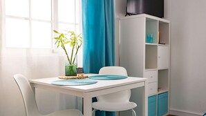 A white table with two chairs, a blue rug, a white cabinet, and a window with blue curtains.