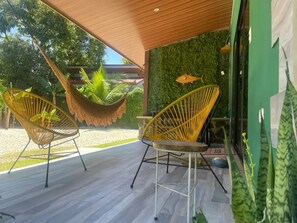 A covered outdoor area with two yellow wicker chairs, a hanging hammock, and a green wall with a fish decoration.