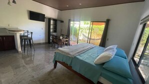 Une chambre à coucher avec un lit, un bureau et une chaise. Une fenêtre offre une vue sur l’extérieur.