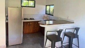 Une cuisine moderne avec un réfrigérateur blanc, des armoires en bois, un plan de travail en marbre et deux tabourets de bar.