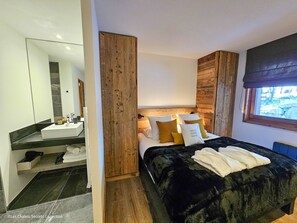 Un dormitorio moderno con una cama grande, un cabecero de madera, un ventanal con vistas y un baño con espejo y lavamanos.