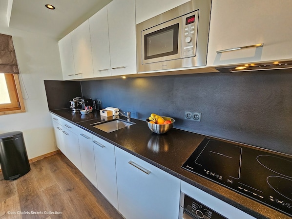 Una cocina moderna con armarios blancos, un microondas de acero inoxidable, una placa de inducción negra y un cuenco de fruta sobre la encimera.