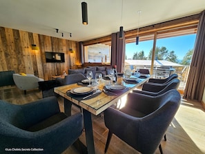 A modern dining area with a long table set for four, surrounded by dark blue upholstered chairs. - Appartement  A-04  T4 (Font-Romeu-Odeillo-Via)