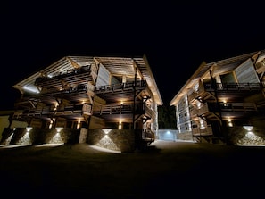 A night view of a traditional wooden chalet with multiple balconies and stone foundations. - Appartement  A-04  T4 (Font-Romeu-Odeillo-Via)