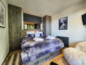 A modern bedroom with a large bed, wooden paneling, a window, and a mounted TV.