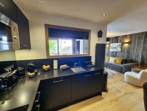 A modern kitchen with a large island, dark cabinetry, and a window above the sink. - Appartement B-03 T2 Cabine (Font-Romeu-Odeillo-Via)