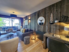 A cozy living area with a wooden accent wall, a sofa, a coffee table, and a dining area with chairs and a lamp.