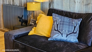 A dark brown sofa with a yellow throw pillow and a blue pillow with a deer design. A small table with a lamp and a black moose figurine is in the background. - Appartement B-12 T2 Cabine (Font-Romeu-Odeillo-Via)