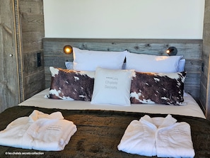 A bed with a wooden headboard, two white pillows, and a pillow with a cow print design. There are two bedside lamps and two towels on the bed. - Appartement B-12 T2 Cabine (Font-Romeu-Odeillo-Via)
