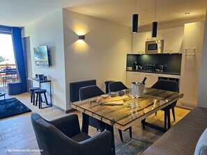 Uma sala de jantar moderna com uma mesa de madeira, cadeiras pretas e uma cozinha ao fundo.