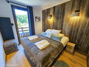 Camera da letto con testiera in legno, letto con lenzuola bianche, due lampade da comodino e vista sull'esterno tramite una porta scorrevole.